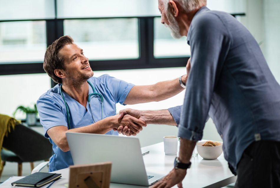 Smiling doctor greeting a mature patient and shaking hands with him at medical clinic.